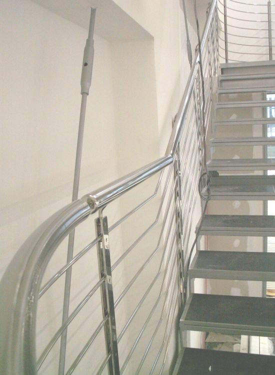 Schody metalowe z balustradą ze stali nierdzewnej, widok z dołu, z widocznym mocowaniem do sufitu.